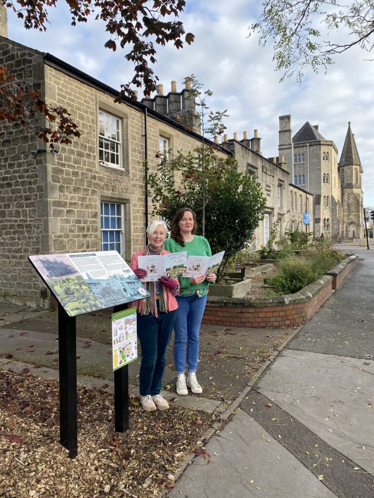 Allie and Hannah follow the Children's Heritage Story Trail in Swindon's Historic Railway Village. They stand at one of the WORKS trail signs, located in front of the Central Community Centre.